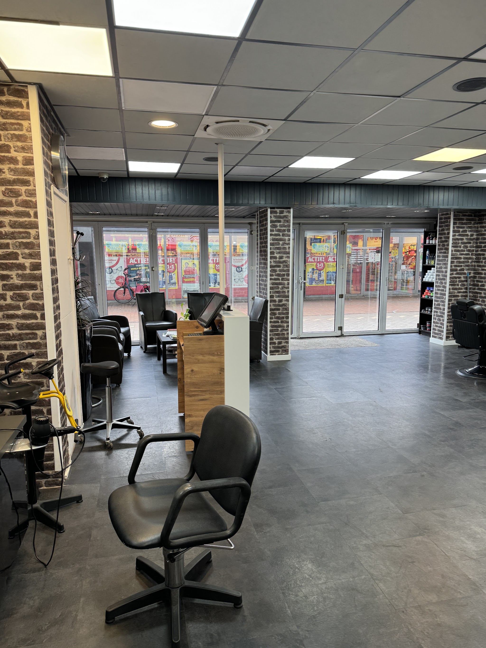 Het interieur van Kapsalon HAKAR met bakstenen pilaren, kappersstoelen en de glazen pui naar het plein