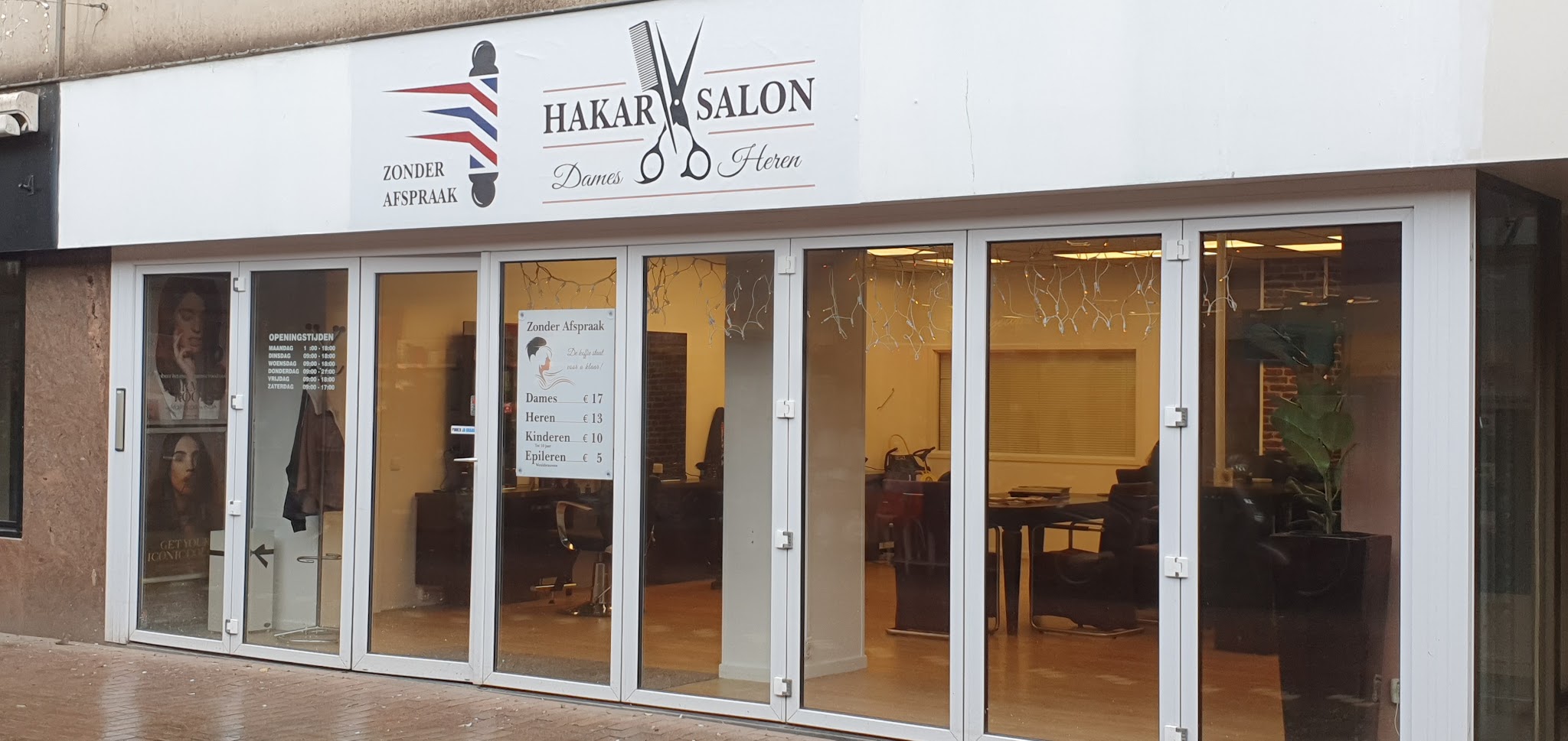 De gevel van Kapsalon HAKAR met het witte bord HAKAR SALON, Zonder afspraak en Dames Heren boven de glazen pui